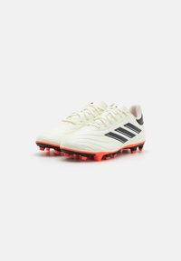 Botas de fútbol con parte superior sintética blanca, tres franjas negras, suela naranja y tracción con tacos negros. Diseño de cierre con cordones.