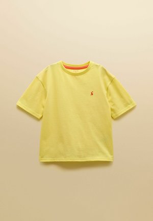 Kollane lühikeste varrukatega ümara kaelusega T-särk, millel on vasakul rinnal väike punane tikandiga logo, esitletud beežil taustal.