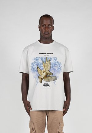 Hvid bomulds t-shirt med et grafisk motiv af en fugl i flugt, omkranset af blå accenter og teksten "VINTAGE DREAMS" ovenfor.
