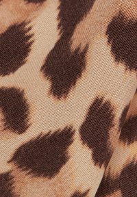 Leopardmönstrad tyg har en beige bakgrund med mörkbruna fläckar. Texturen är slät med ett subtilt vävmönster.