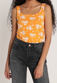 Débardeur floral orange avec un col carré, associé à un jean gris foncé taille haute doté de poches avant et d'un bouton en métal.