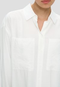 White button-up shirt with a classic collar, featuring two chest pockets, made from a lightweight, slightly textured fabric.