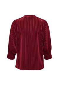 Blusa de terciopelo rojo con una textura acanalada vertical, escote redondo y mangas abullonadas de tres cuartos con puños elásticos.
