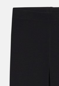 Leggings noirs avec une texture côtelée et une coupe ajustée. Présentent une taille sans couture et un léger détail fendu à la cheville.