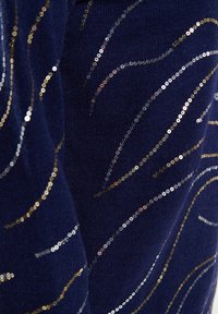Marineblauer Stoff, verziert mit goldenen, silbernen und roségoldenen Pailletten, die in wellenförmigen Mustern angeordnet sind und so visuelles Interesse und Glanz erzeugen.