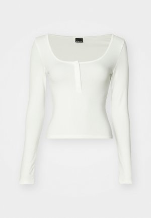 Blusa branca de mangas longas com decote redondo e uma única linha de botões. Feita de tecido suave com um corte ajustado e sem padrões visíveis.