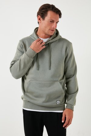Sudadera verde hecha de un tejido suave y texturizado, con un bolsillo canguro, capucha con cordón y un pequeño parche con el logo en la parte inferior delantera.