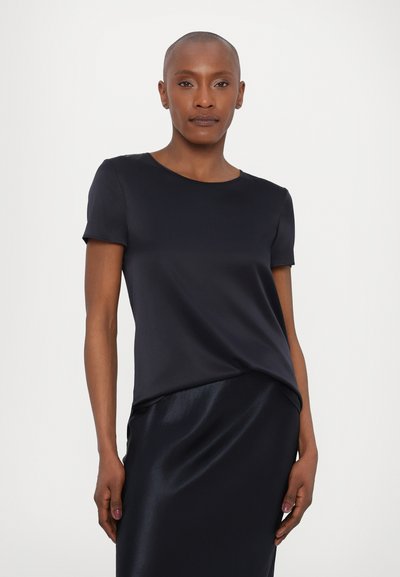 Mornarsko modra majica s kratkimi rokavi iz gladkega materiala z okroglo izreza, v kombinaciji z usklajenim satenskim krilom. Ima drapirano sprednjo podrobnost.