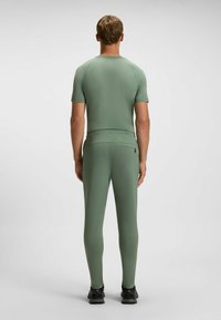 Fitted athletic outfit in muted green, featuring short sleeves, stretchy material, and a waistband pocket. Smooth texture and streamlined design.