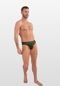 Groene katoen boxershorts met een logo tailleband, met een lage taille en een gladde textuur. Model staat blote voeten op een neutrale achtergrond.