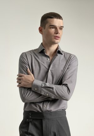 Camisa de botones gris claro con cuello, que presenta una textura sutil y costuras visibles, combinada con pantalones gris oscuro con detalles de botones.