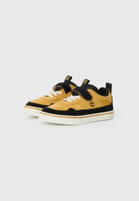Yellow suede sneakers with black accents, white laces, and a rubber sole. Features a Velcro strap and a logo on the side.