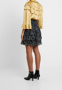 Blusa gialla a volant con maniche lunghe abbinata a una gonna nera a strati con stampa floreale. Completata da stivaletti neri alla caviglia.