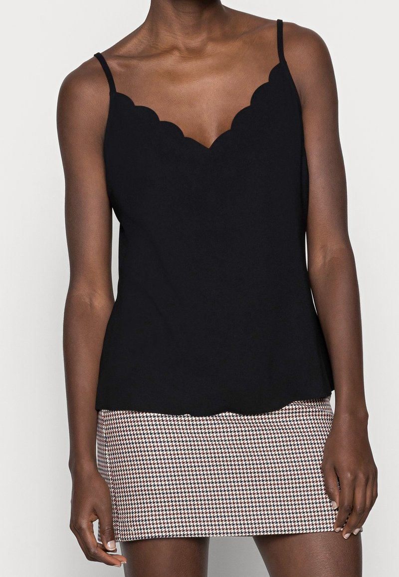 Haut sans manches noir avec un décolleté en coquille, réalisé dans un tissu doux ; superposé à une mini-jupe ajustée à motif pied-de-poule.