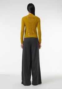 Senfgelbes Sweatshirt mit einem Pailletten-Rückenteil, kombiniert mit lockeren, dunkelgrauen, weit geschnittenen Hosen. Glatte Textur, enganliegende Ärmel.