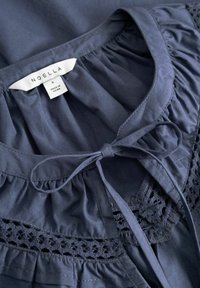 Tmavě modrá halenka s volánkovým límcem, zavazovacím mašlí u výstřihu a krajkovým lemováním, s označením značky "Noella" uvnitř límce.