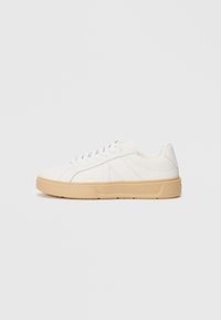 Hvit sneakers med en teksturert, lys beige såle. Har en glatt læroverdel og snøring med subtil merking på siden.