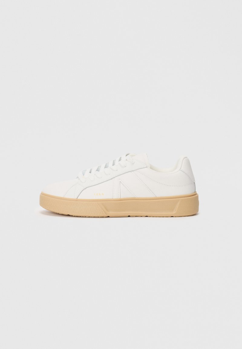 Hvit sneakers med en teksturert, lys beige såle. Har en glatt læroverdel og snøring med subtil merking på siden.