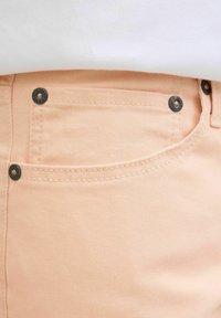 Hlače od pamuka breskvaste boje s vidljivim šavovima, prednjim džepom i metalnim dodacima s branded detaljima. Glatka tekstura.