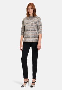 Langarmige top met een patroon in beige, marineblauw en wit, met een hoge hals. Gecombineerd met zwarte slim-fit broek en bicolor hoge hakken.