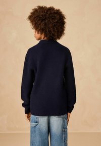 Marineblauer gestrickter Pullover mit strukturiertem Muster und langen Ärmeln, kombiniert mit locker sitzenden hellblauen Denim-Cargohosen.