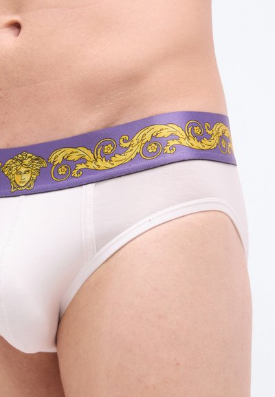 Λευκά βαμβακερά εσώρουχα με μοβ ελαστική μέση που διαθέτει χρυσό μπαρόκ μοτίβο και έμβλημα Μέδουσας· ομαλή υφή, εφαρμοστή γραμμή.
