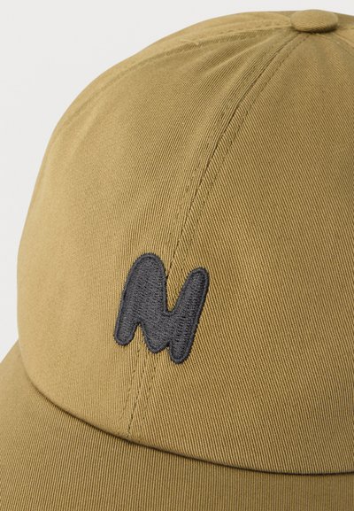 Casquette de baseball marron clair avec une lettre "M" noire brodée sur le panneau avant, montrant la texture du tissu et les détails de la couture.