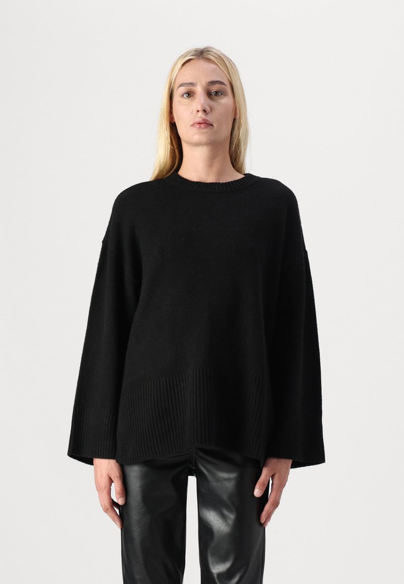 Oversized svart genser laget av mykt materiale med ribbestrikket kant og vide ermer, kombinert med skinnende svarte skinnbukser.