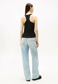 Top senza maniche nero con design a racerback, abbinato a jeans a gamba larga di un blu chiaro. Il tessuto è liscio con una leggera lucentezza. Calzature nere.