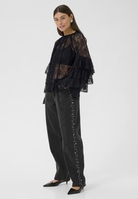 Melna mežģīņu blūze ar kārtotiem volāniem, kopā ar tumšām džinsām ar kniedēm sānos un melniem smailiem papēžiem.