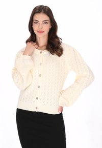 Kremowy sweter z dzianiny, ozdobiony teksturowym wzorem w diamenty, z bufiastymi rękawami i okrągłymi guzikami. Posiada prążkowane mankiety i dół.