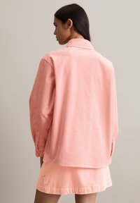 Roze corduroy blouse met een kraag, doorlopende schouders en een losse pasvorm, gecombineerd met een bijpassende corduroy rok met verticale ribbelstructuur.