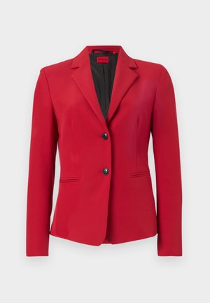 Red blazer with a structured design, single-breasted with two buttons, peaked lapels, and side pockets; smooth texture and sleek silhouette.