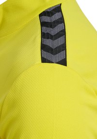 Gul atletikshirt med tekstureret stof, der har en sort panel og mønstrede detaljer langs skulderen for ekstra designelement.