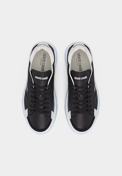 Ζευγάρι μαύρα και άσπρα δερμάτινα αθλητικά παπούτσια με κορδόνια, με την επωνυμία «roberto cavalli» στη γλώσσα και στην ενδιάμεση σόλα, φαίνονται από πάνω σε λευκό φόντο.