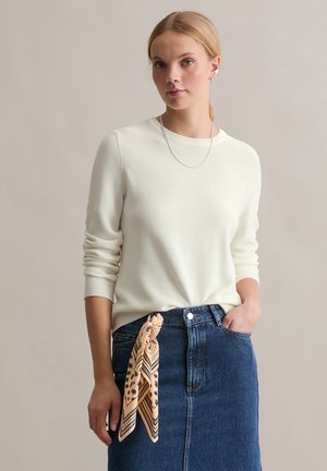 Cream-colored knit sweater with long sleeves, paired with a denim skirt featuring a tied striped and floral patterned scarf at the waist.