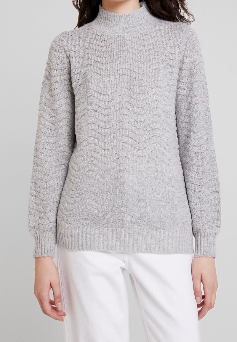 Pull en maille gris clair avec un motif texturé en forme de vague, col montant, poignets et ourlet côtelés. Tissu doux de poids moyen.