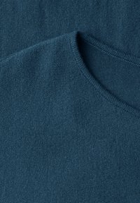Gros plan sur un tissu tricoté bleu sarcelle foncé présentant un col rond avec une fine couture côtelée et une surface texturée.