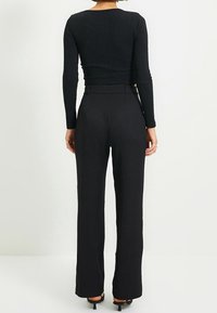 Haut noir à rayures en maille à manches longues associé à un pantalon noir taille haute. Le pantalon a une coupe ajustée et des jambes droites.