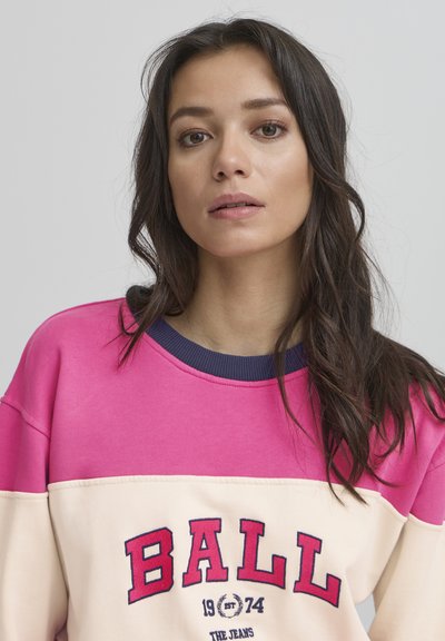 Rozā un krēmkrāsas džemperis ar tumši zilu apkakli, ar drosmīgu "BALL 1974" logo tumši sarkanā krāsā un brīvu piegriezumu.