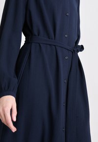 Navy blue shirt dress in lightweight fabric, featuring a button front, belted waist, and long sleeves with gathered cuffs.