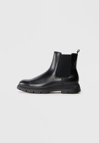 Botas Chelsea de cuero negro con paneles elásticos, punta redonda y suela de goma texturizada. Presenta un tirador en la parte trasera para facilitar el calzado.