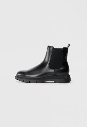 Botas Chelsea de cuero negro con paneles elásticos, punta redonda y suela de goma texturizada. Presenta un tirador en la parte trasera para facilitar el calzado.