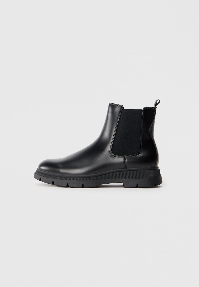 Botas Chelsea de cuero negro con paneles elásticos, punta redonda y suela de goma texturizada. Presenta un tirador en la parte trasera para facilitar el calzado.