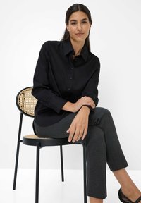 Camicia nera con bottoni realizzata in tessuto liscio, caratterizzata da maniche lunghe e colletto classico, abbinata a pantaloni fitted grigi scuri.