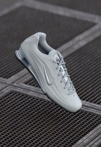 Light gray Nike running shoe with swoosh logo, textured upper, and laces, positioned above a metal grid surface.
