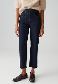 Dark blue high-waisted jeans with a straight fit, frayed hem, and copper stitching. Paired with dark burgundy loafers.