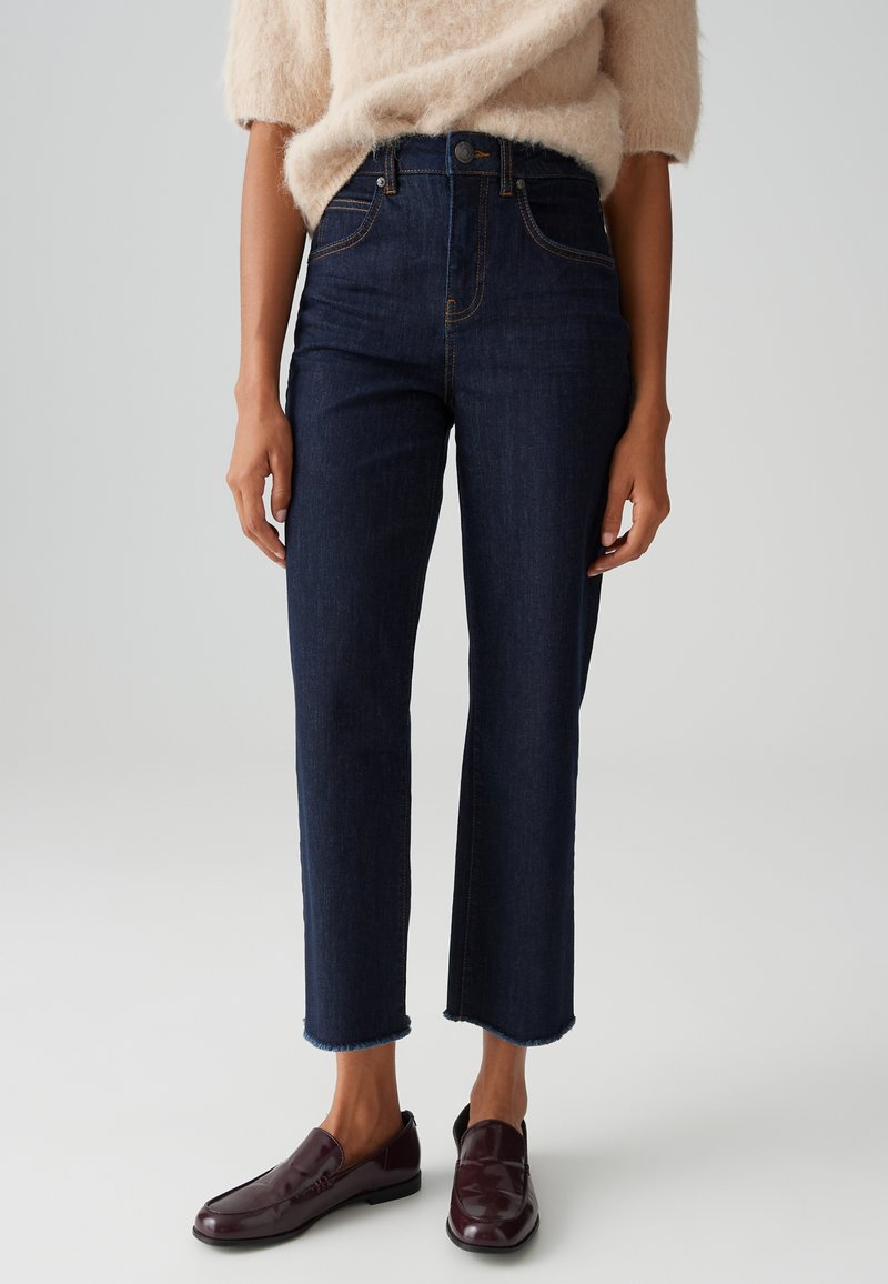 Dark blue high-waisted jeans with a straight fit, frayed hem, and copper stitching. Paired with dark burgundy loafers.