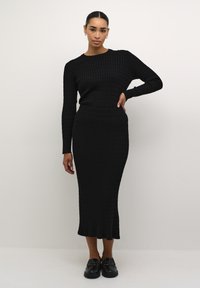 Ensemble de pull en maille côtelée noire et jupe midi au design ajusté ; la jupe présente un ourlet évasé, associé à des mocassins noirs brillants.