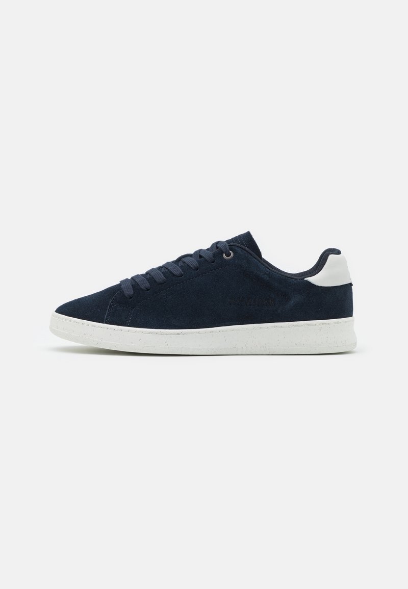 Baskets basses en daim bleu marine avec semelle en caoutchouc blanche et accent blanc au talon, vues de côté sur un fond uni.